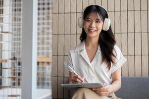 a atraente ásia mulher ouvindo para música enquanto trabalhando em dela digital tábua dentro uma cafeteria. foto