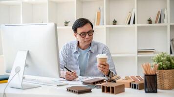 uma Senior masculino interior desenhador é bebericando café enquanto trabalhando em dele projeto dentro a escritório. foto