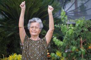 retrato do a idosos mulher exercício enquanto em pé dentro uma jardim. uma lindo Senior mulher curto com cinzento cabelo é feliz e saudável. conceito do envelhecido pessoas e cuidados de saúde foto