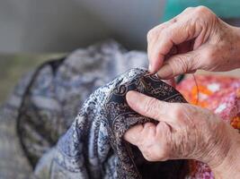 fechar-se do mãos Senior mulher usando agulha e fio para emendar uma calça. seletivo foco. conceito do envelhecido pessoas e feito à mão foto