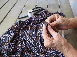fechar-se do mãos Senior mulher tentando para fio uma agulha para de costura pano. espaço para texto. conceito do envelhecido pessoas e relaxamento foto