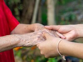 fechar-se do uma jovem mulher mãos segurando a idosos feminino mãos. conceito do envelhecido pessoas e cuidados de saúde foto