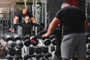 fitness, Esportes, exercícios e levantamento de peso. conceito - uma jovem mulher e uma jovem homem com halteres varrendo músculos dentro a Academia foto