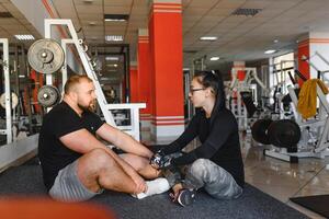 fitness, Esportes, exercícios e levantamento de peso. conceito - uma jovem mulher e uma jovem homem com halteres varrendo músculos dentro a Academia foto