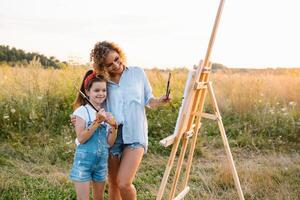 mãe ensina filha pintura dentro parque. ensolarado natureza, mãe e filha pintura uma cenário dentro uma parque , pintura uma pequeno criança, criança criatividade. mãe dia. foto