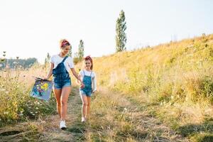 beleza mãe pintura com dela pequeno filha. à moda mulher desenhando a cenário com pequeno garota. fofa criança dentro uma branco camiseta e azul jeans. mãe dia. foto