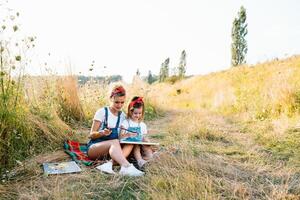 beleza mãe pintura com dela pequeno filha. à moda mulher desenhando a cenário com pequeno garota. fofa criança dentro uma branco camiseta e azul jeans. mãe dia. foto