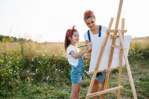 mãe ensina filha pintura dentro parque. ensolarado natureza, mãe e filha pintura uma cenário dentro uma parque , pintura uma pequeno criança, criança criatividade. mãe dia. foto