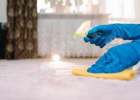 pessoas, tarefas domésticas e serviço de limpeza conceito - fechar acima do mulher dentro borracha luvas com pano e derergente spray limpeza tapete às lar. fechar acima do mulher com pano limpeza tapete foto