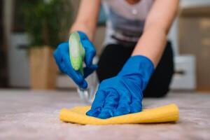 pessoas, tarefas domésticas e serviço de limpeza conceito - fechar acima do mulher dentro borracha luvas com pano e derergente spray limpeza tapete às lar. fechar acima do mulher com pano limpeza tapete foto