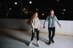 inverno patins, amoroso casal segurando mãos e rolando em pista. iluminação dentro fundo, noite. conceito treinamento. foto