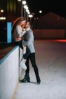 jovem casal dentro amor, encontro às a gelo pista, uma menina sentado em uma guarda corpo e beijo com dela namorado. foto