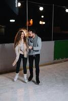 homem e mulher jovem família feliz sorrisos aguarde mãos patim em inverno rinque às noite, com bokeh luzes. foto