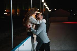 jovem casal dentro amor, encontro às a gelo pista, uma menina sentado em uma guarda corpo e beijo com dela namorado. foto