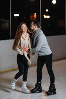 inverno patins, amoroso casal segurando mãos e rolando em pista. iluminação dentro fundo, noite. conceito treinamento. foto