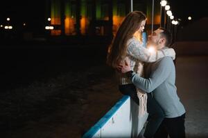 tema gelo patinação rinque e amoroso casal. encontro jovem, à moda pessoas passeio de mão dentro multidão em cidade patinação rinque aceso de luz lâmpadas e luzes. gelo patinação dentro inverno para Natal em gelo arena. foto