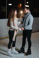 inverno patins, amoroso casal segurando mãos e rolando em pista. iluminação dentro fundo, noite. conceito treinamento. foto