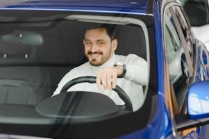 jovem bonito homem escolhendo uma carro dentro uma carro sala de exposições foto