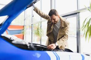 visitando carro concessionária. bonito barbudo homem é acariciando dele Novo carro e sorridente foto