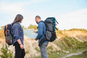 lindo casal do uma Viajantes estão procurando caminho em localização mapa enquanto em pé em Alto Colina dentro ensolarado dia, masculino e fêmea caminhantes estão caminhando juntos dentro montanhas durante grandes aguardando verão final de semana foto