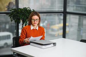 retrato do uma feliz casual empresária dentro suéter sentado às dela local de trabalho dentro escritório foto