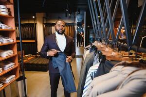 uma à moda elegantemente vestido afro-americano homem trabalhando às clássico roupa masculina loja. foto