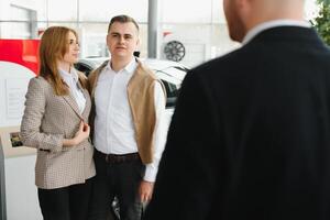 feliz jovem casal escolhe e comprando uma Novo carro para a família dentro a concessionária foto