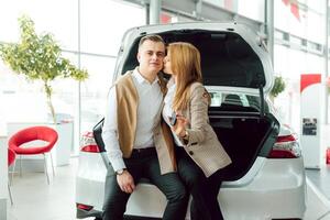 visitando carro concessionária. lindo casal é segurando uma chave do seus Novo carro e sorridente, menina é se beijando dela marido dentro bochecha. foto