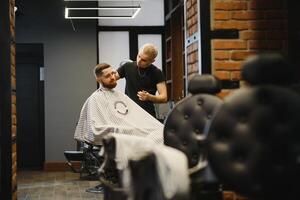 jovem bonito barbeiro fazer corte de cabelo do atraente barbudo homem dentro barbearia. foto