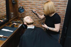 mulher barbeiro corte cabelo para uma barbudo cara. foto