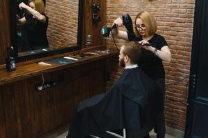 barbeiro mulher corte homem cabelo às a barbearia. mulher trabalhando Como uma cabeleireiro. pequeno o negócio conceito foto