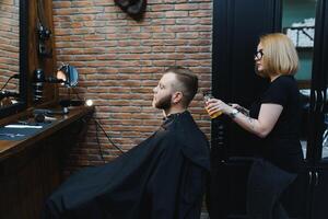 servindo cliente dentro barbearia. profissional barbeiro garota, fêmea cabeleireiro fazer moderno corte de cabelo para uma homem sentado dentro barbeiro fazer compras cadeira. foco em uma garota. cabeleireiro, barbear, corte, aliciamento foto