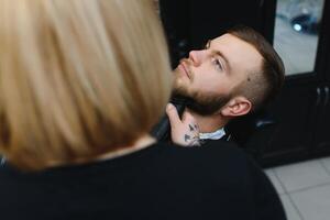 barbearia ou cabeleireiro conceito. mulher cabeleireiro cortes barba com tesoura. homem com grandes barba, bigode e à moda cabelo. cara com moderno Penteado visitando cabeleireiro foto