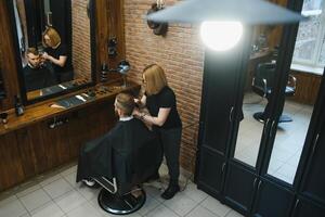 à moda homem sentado barbeiro fazer compras estilista de cabelo cabeleireiro mulher corte dele cabelo retrato bonito feliz jovem barbudo caucasiano cara obtendo na moda corte de cabelo atraente barbeiro menina trabalhando servindo cliente. foto