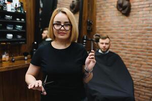 retrato do moda mulher barbeiro estilista de cabelo com tesouras dentro mão dentro a barbearia foto