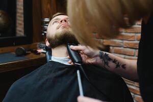 especializado fêmea barbeiro corte uma barba do morena adulto cara dentro profissional retro barbearia. foto