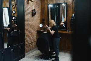 à moda homem sentado barbeiro fazer compras estilista de cabelo cabeleireiro mulher corte dele cabelo retrato bonito feliz jovem barbudo caucasiano cara obtendo na moda corte de cabelo atraente barbeiro menina trabalhando servindo cliente foto