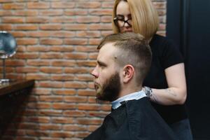 barbeiro mulher corte homem cabelo às a barbearia. mulher trabalhando Como uma cabeleireiro. pequeno o negócio conceito. foto