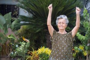 retrato do a idosos mulher exercício enquanto em pé dentro uma jardim. uma lindo Senior mulher curto com cinzento cabelo é feliz e saudável. conceito do envelhecido pessoas e cuidados de saúde foto