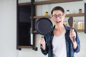 jovem do homem em pé segurando a panela e concha. ele é olhando às a Câmera e sorridente dentro dele cozinha para preparado para cozinhar com uma feliz. positivo pensando para uma feliz vida. feliz vida conceito foto