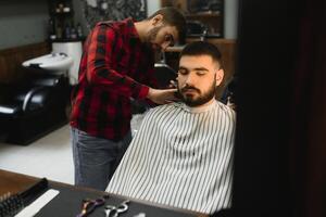 sério jovem barbudo homem obtendo corte de cabelo de barbeiro. barbearia tema. foto