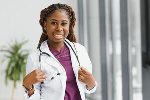 retrato do fêmea africano americano médico em pé dentro dela escritório às clínica. foto