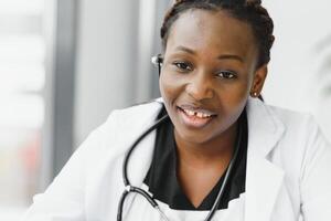 fechar-se retrato do amigável, sorridente confiante fêmea cuidados de saúde profissional com laboratório casaco, estetoscópio, braços cruzado. isolado hospital clínica fundo. Tempo para a escritório Visita. foto