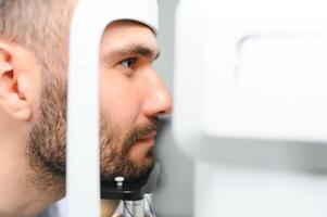bonito jovem homem é verificação a olho visão dentro moderno oftalmologia clínica. paciente dentro oftalmologia clínica foto