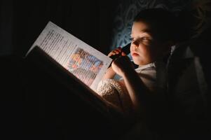 criança lendo livro dentro cama. crianças ler às noite. pequeno Garoto com fada conto livros dentro quarto . Educação para jovem crianças. hora de dormir história dentro a tarde. fofa criança debaixo cobertor dentro Sombrio quarto com luminária foto