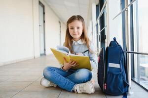 frente Visão do bonita Loiras escola menina segurando muitos colorida notas e livros. esperto adolescente menina sorridente às Câmera, em pé em corredor do internacional escola. foto