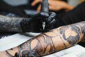 cortada fechar acima do uma barbudo tatuagem artista trabalhando às dele estúdio tatuagem manga em a braço do dele masculino cliente. homem obtendo tatuado de profissional tatuador foto