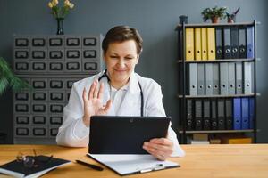 Tiros na Cabeça retrato inscrição tela Visão do meia idade fêmea médico ou gp conversa consultar cliente conectados em computador, mulher enfermeira falar com doente paciente em ligar usar Webcam conferência em computador portátil foto