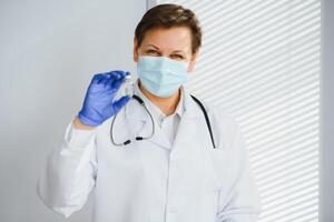 fechar-se mão do mulher médico ou cientista dentro médico uniforme vestindo face mascarar protetora dentro laboratório segurando remédio líquido vacinas frasco garrafa, coronavírus ou covid-19 conceito. foto