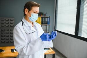 retrato do uma fêmea médico vestindo face mascarar e segurando dela paciente gráfico em digital tábua enquanto em pé às a hospital. foto